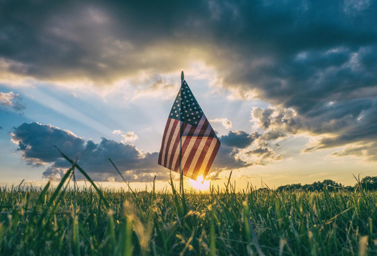 American flag standing in a grass field with sunset in background